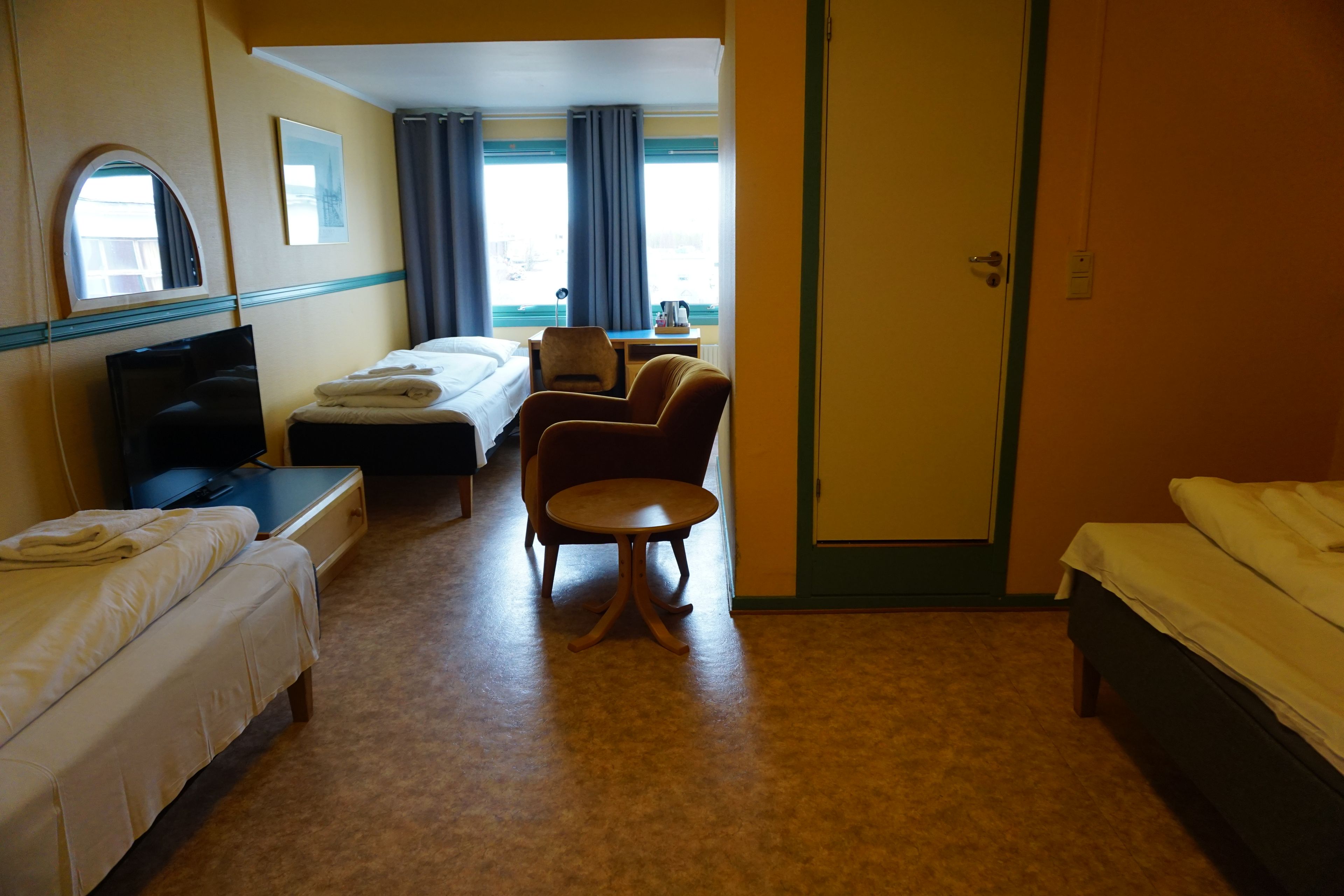 A hotel room with two beds, a desk, a chair, and a television.