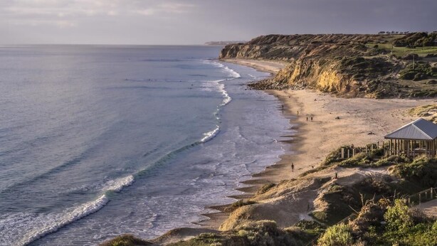 A coastal landscape with a sandy beach, a rocky cliff, and a small wooden structure. - Fleurieu Eco Escape - Luxurious, Stylish, Cosy and Clean Hideaway (Aldinga)