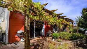 A residential garden with a pergola covered in grapevines, a red garage, and a wooden deck. - Fleurieu Eco Escape - Luxurious, Stylish, Cosy and Clean Hideaway (Aldinga)
