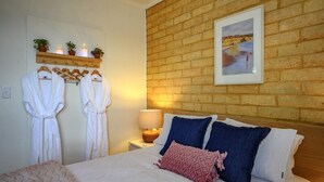 A hotel room with a brick wall, a bed with blue and white pillows, a bedside lamp, and a framed picture on the wall. - Fleurieu Eco Escape - Luxurious, Stylish, Cosy and Clean Hideaway (Aldinga)