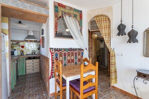 Una cocina compacta con zona de comedor, mantel estampado y una lámpara colgante tradicional.