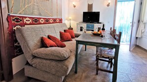 Een woonkamer met een bank, een eettafel, een televisie en een wand met een decoratief wandtapijt.