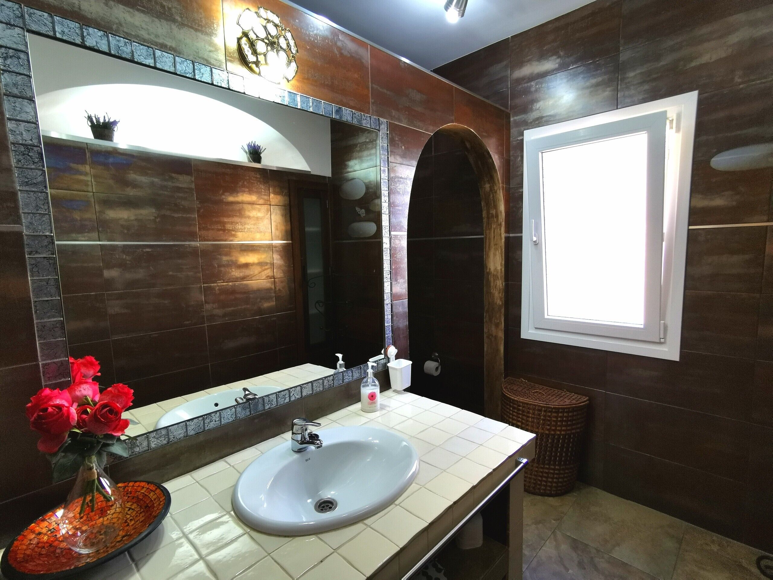 A bathroom with a white sink, a mirror, a potted plant, and a window.