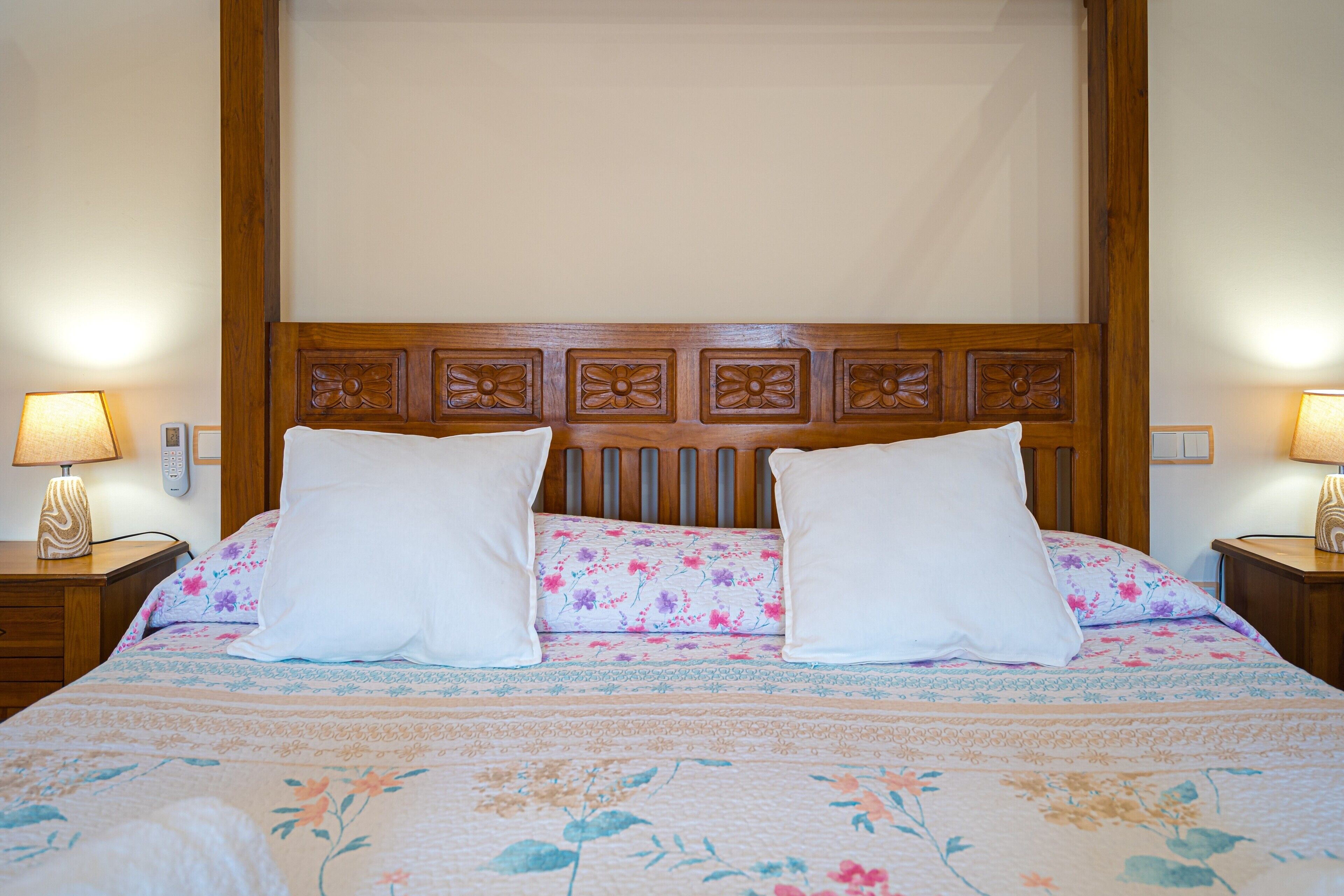Un lit recouvert d’une couvre-lit à motifs floraux, avec deux oreillers blancs et une tête de lit en bois ornée de sculptures florales.