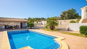 Une piscine avec une terrasse carrelée, un espace de repos couvert et un bâtiment doté d’un toit en tuiles.