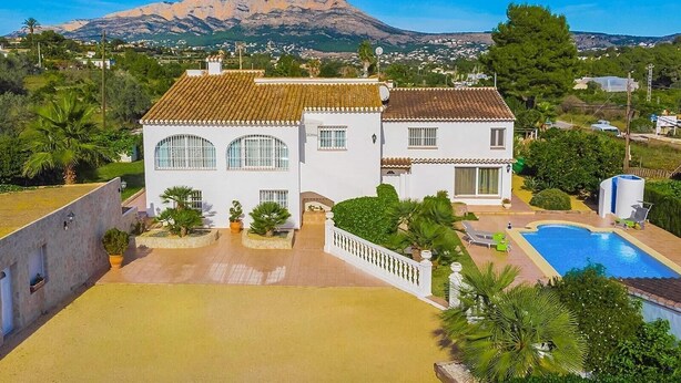 Une maison à deux étages, avec un toit en tuiles, une piscine et une vue sur une montagne.