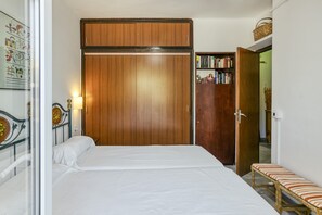 A bedroom with a bed, a wooden wardrobe, a bench, and a bookshelf.