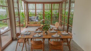 Ein Essbereich mit Holztisch, gedeckt für vier Personen, umgeben von großen Fenstern mit Blick auf den Garten.