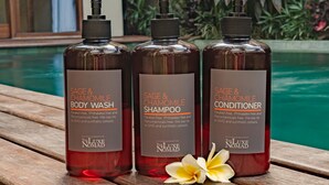 Drei Flaschen Duschgel, Shampoo und Conditioner stehen auf einem Holztisch in Poolnähe.