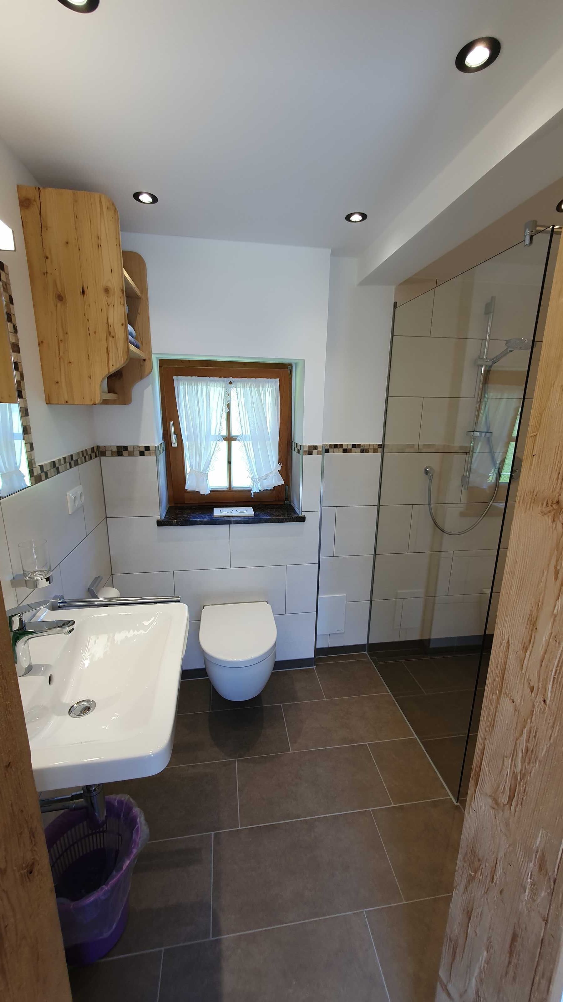 Een badkamer met een wastafel, toilet, douche en houten kastjes.