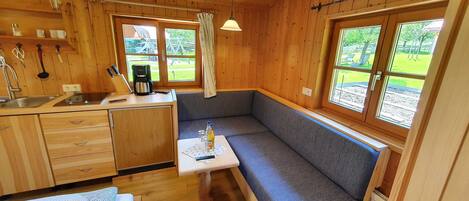 Una cabaña acogedora con kitchenette, comedor con banco y grandes ventanales con vistas al exterior.