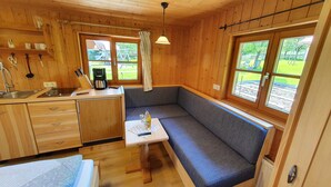 A compact cabin with a kitchenette, a dining area with a bench, and large windows offering a view of the outdoors.