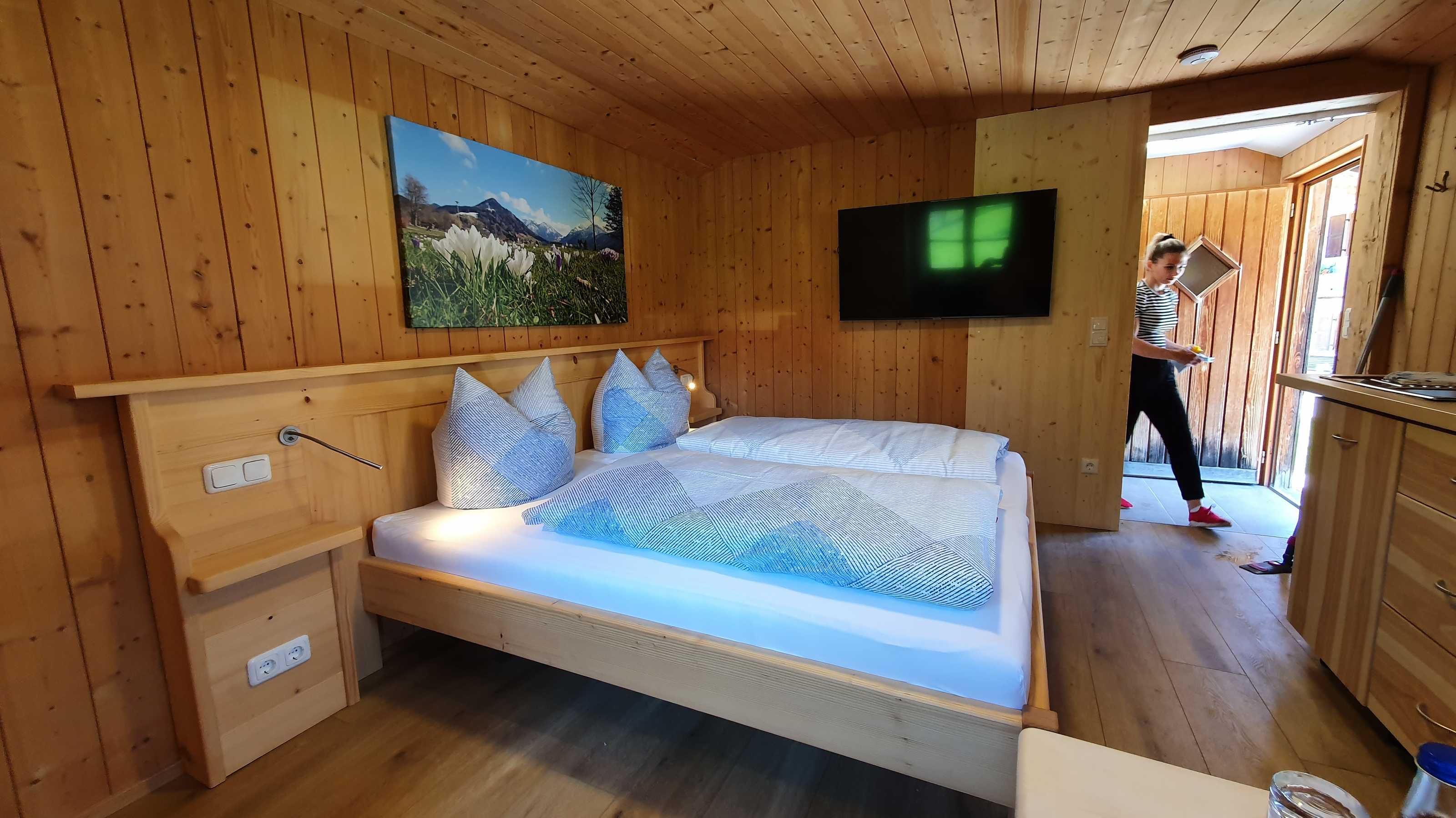 A wooden-paneled room with a bed, a TV, and a painting on the wall.