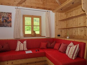 A cozy room with a red sofa, wooden shelves, a window with curtains, and a painting on the wall. - Ferienhaus Brecherspitz - Der Anderlbauer am See (Schliersee)