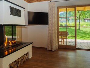 A modern living room with a fireplace, a flat-screen TV, and a sliding glass door leading to an outdoor patio. - Ferienhaus Brecherspitz - Der Anderlbauer am See (Schliersee)