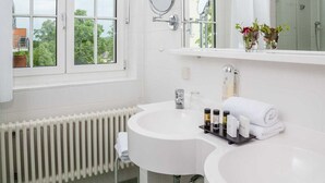 Un bany amb un lavabo blanc, un mirall i una finestra amb vista a arbres.