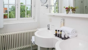 A bathroom with a white sink, a mirror, and a window with a view of trees.