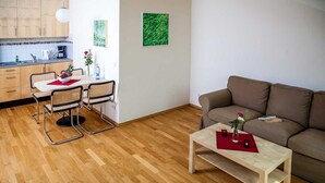 Uma sala de estar moderna com um sofá marrom, uma mesa de centro de madeira e um espaço de jantar com cadeiras de vime e uma mesa branca.