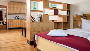 A hotel room with a bed, a wooden wardrobe, a small table, and a kitchenette.