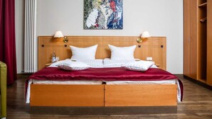 Een tweepersoonsbed met een houten hoofdbord, twee bedlampjes en een rode plaid.