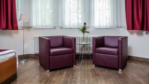 Een kamer met twee paarse fauteuils, een kleine ronde tafel met een bloevas, en een radiator.