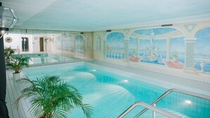 Una piscina interior con un mural de escena clásica, paredes de azulejos y una vista despejada de la piscina.