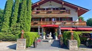 Un hotel con toldo rojo, mesas al aire libre y una fuente.