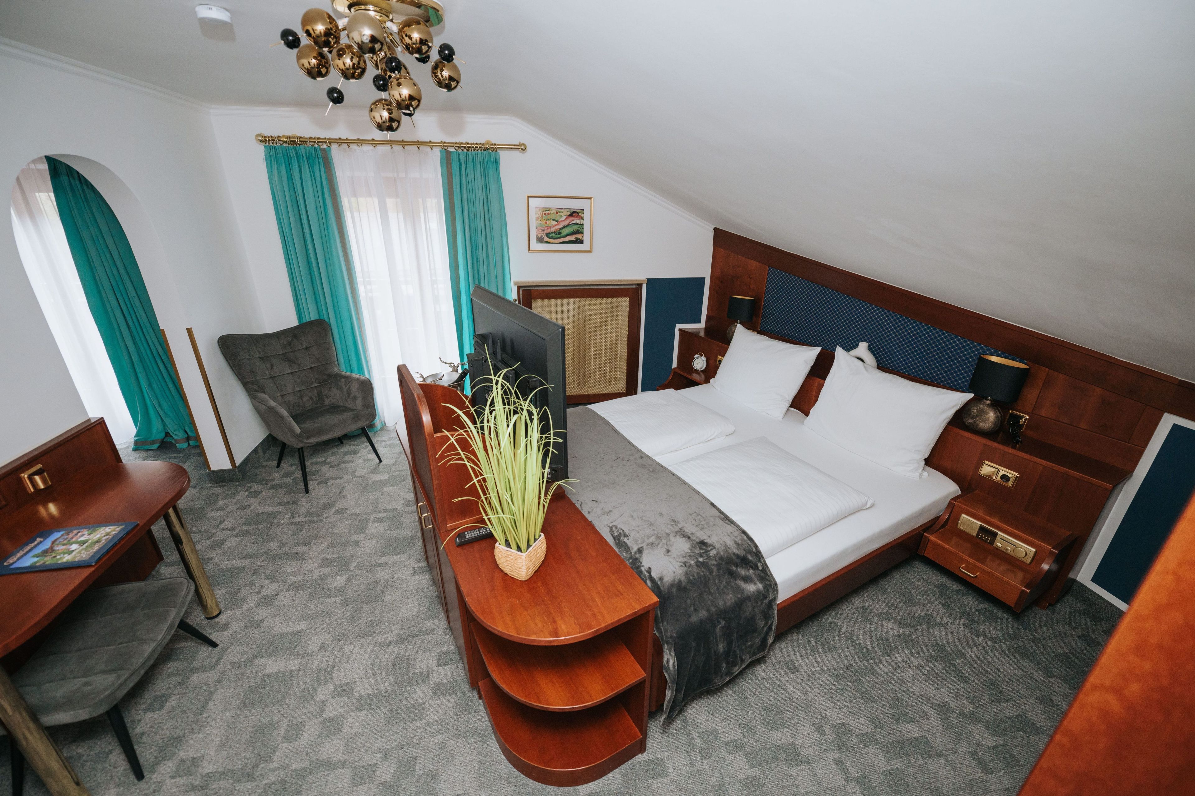Habitación de hotel con cama, escritorio con silla, televisor, mesita de noche y estante en la pared.