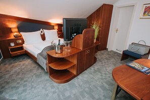 Hotelkamer met een bed, een houten bureau, een klein tafeltje, een televisie, een minibar en een deur.