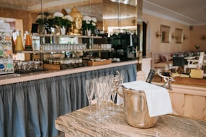 A bar area with a marble countertop, a silver pitcher with a white napkin, and several empty glasses.