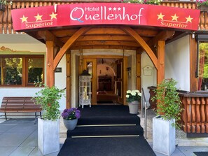 A hotel entrance with a wooden archway, a black carpeted staircase, and potted plants.