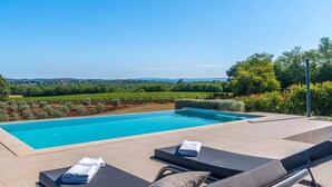 Un espace aménagé au bord de la piscine, avec deux chaises longues, une piscine à l’eau cristalline et une vue sur un vignoble.