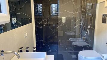 Ein modernes Badezimmer mit einem großen Spiegel, weißen Armaturen und einer Glastür zum Duschbereich.