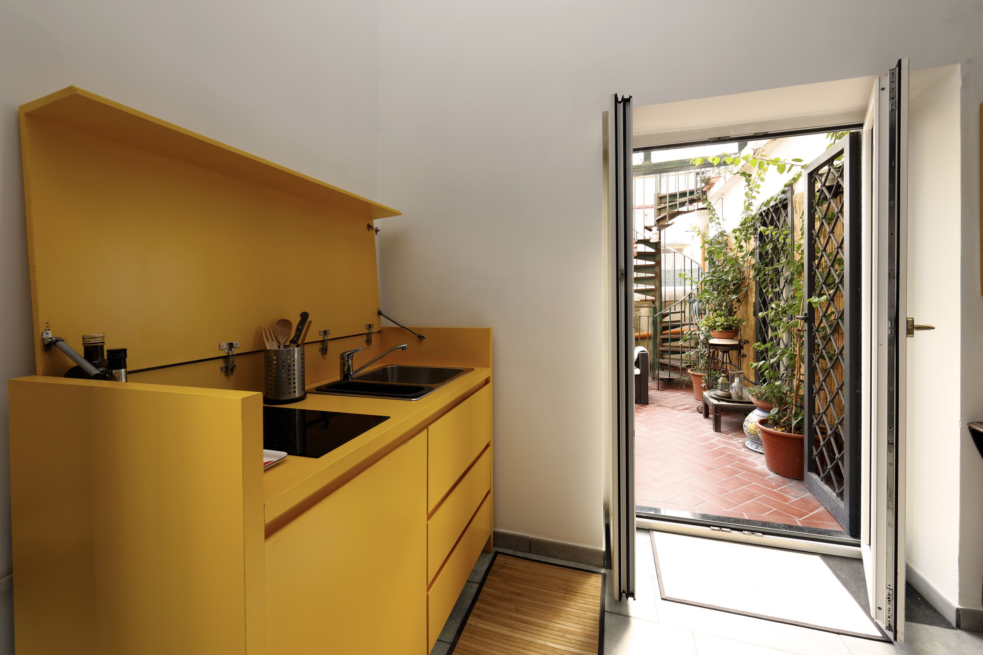 Een kleine keuken met een geel aanrecht en een schuifdeur naar een patio vol potplanten.