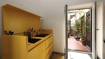 Een kleine keuken met een geel aanrecht en een schuifdeur naar een patio vol potplanten.