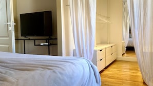 Et soveværelse med seng, fjernsyn på et stativ, et skab og en garderobe.