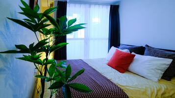 Une chambre d’hôtel avec un lit, une grande fenêtre avec des rideaux et une plante en pot.