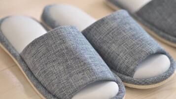 A pair of grey, woven slippers with a white interior, placed on a wooden floor.