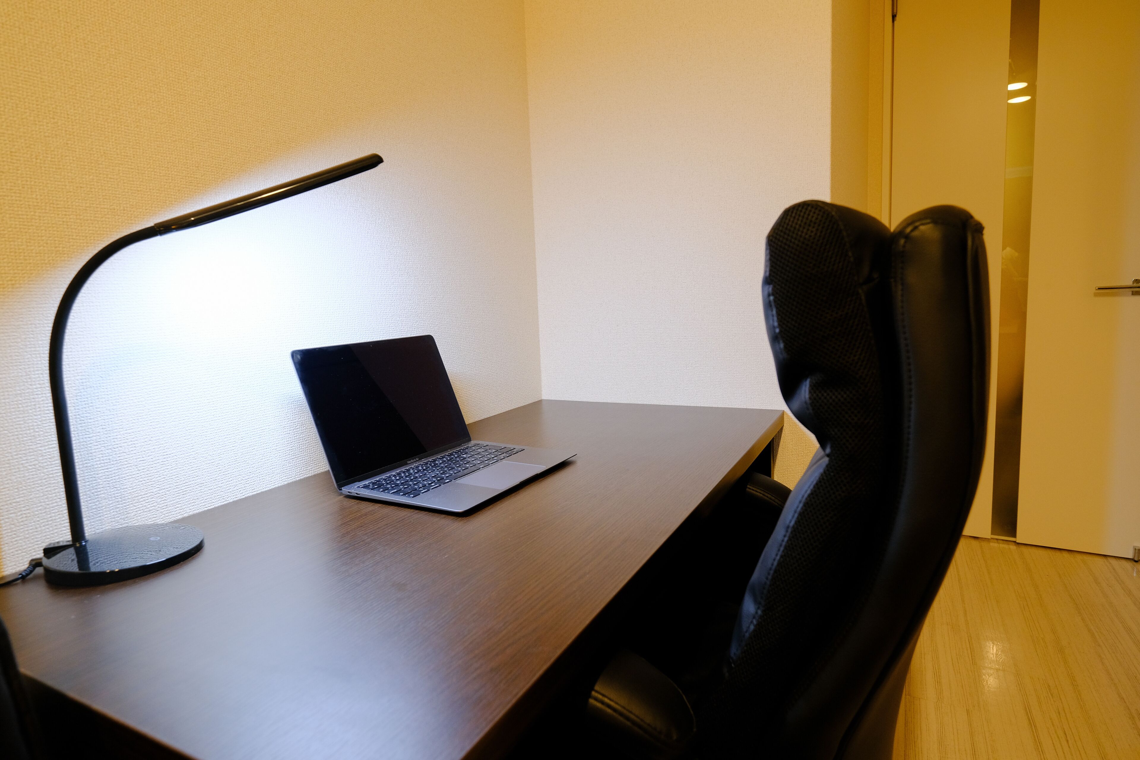A wooden desk with a laptop and a black desk lamp.