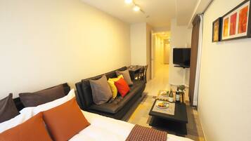 A hotel room with a bed, a sofa, a small table with a bottle and a plate, and a TV on the wall.