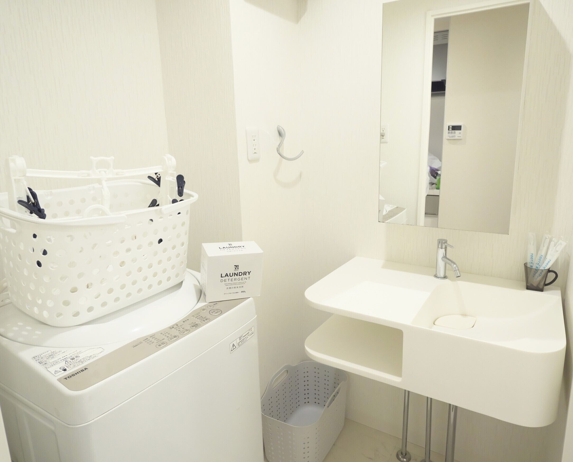 Un bagno con un lavandino bianco, uno specchio, una lavatrice e un cesto per la biancheria.