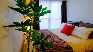 A hotel room with a bed, a large window with curtains, and a potted plant.