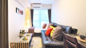 A compact living space with a sofa, a small dining table, and a window providing natural light. - Kicon Hotels Fuchsia (Nagoya)