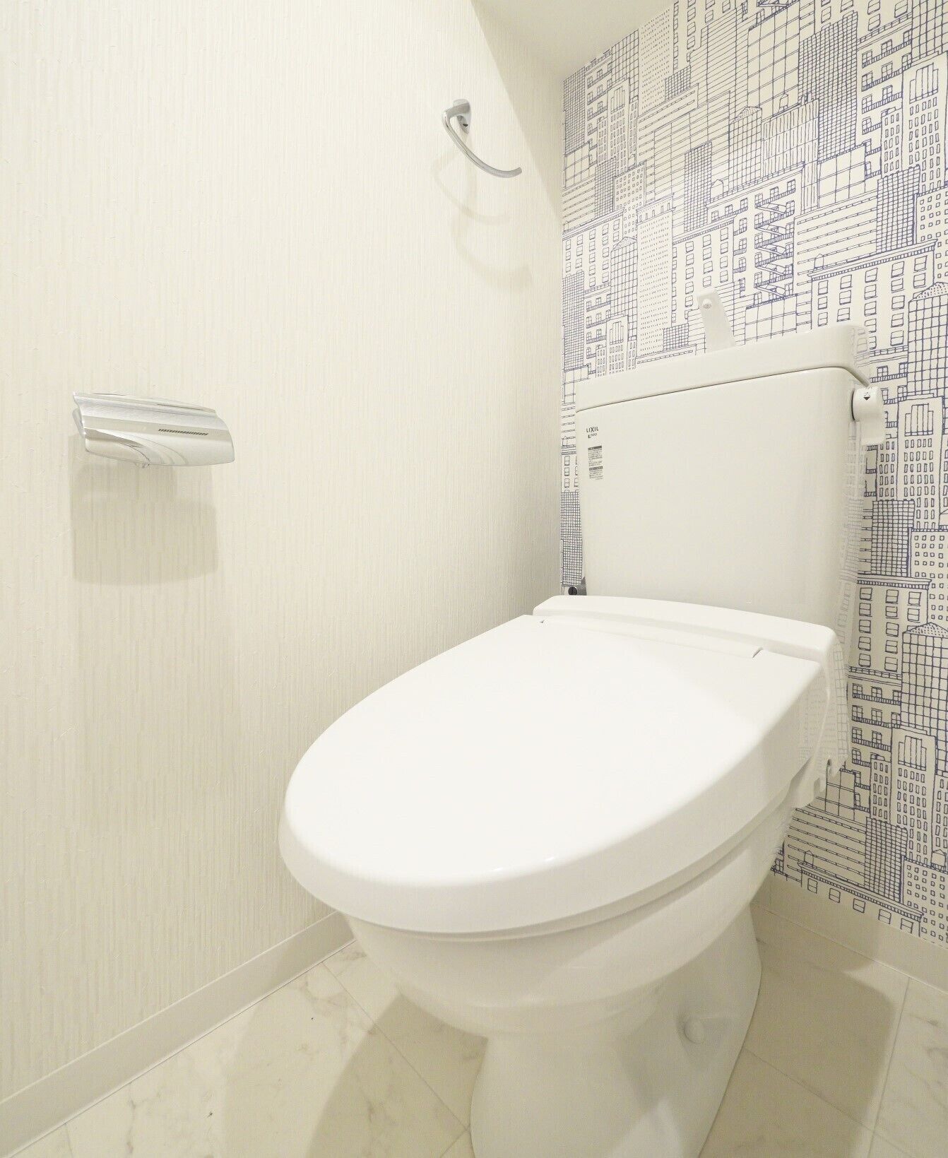 Une salle de bain avec des toilettes blanches, un porte-serviettes et un mur à motifs.