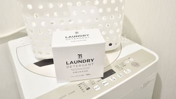 A white laundry detergent box on a washing machine with a white perforated basket containing clothespins.