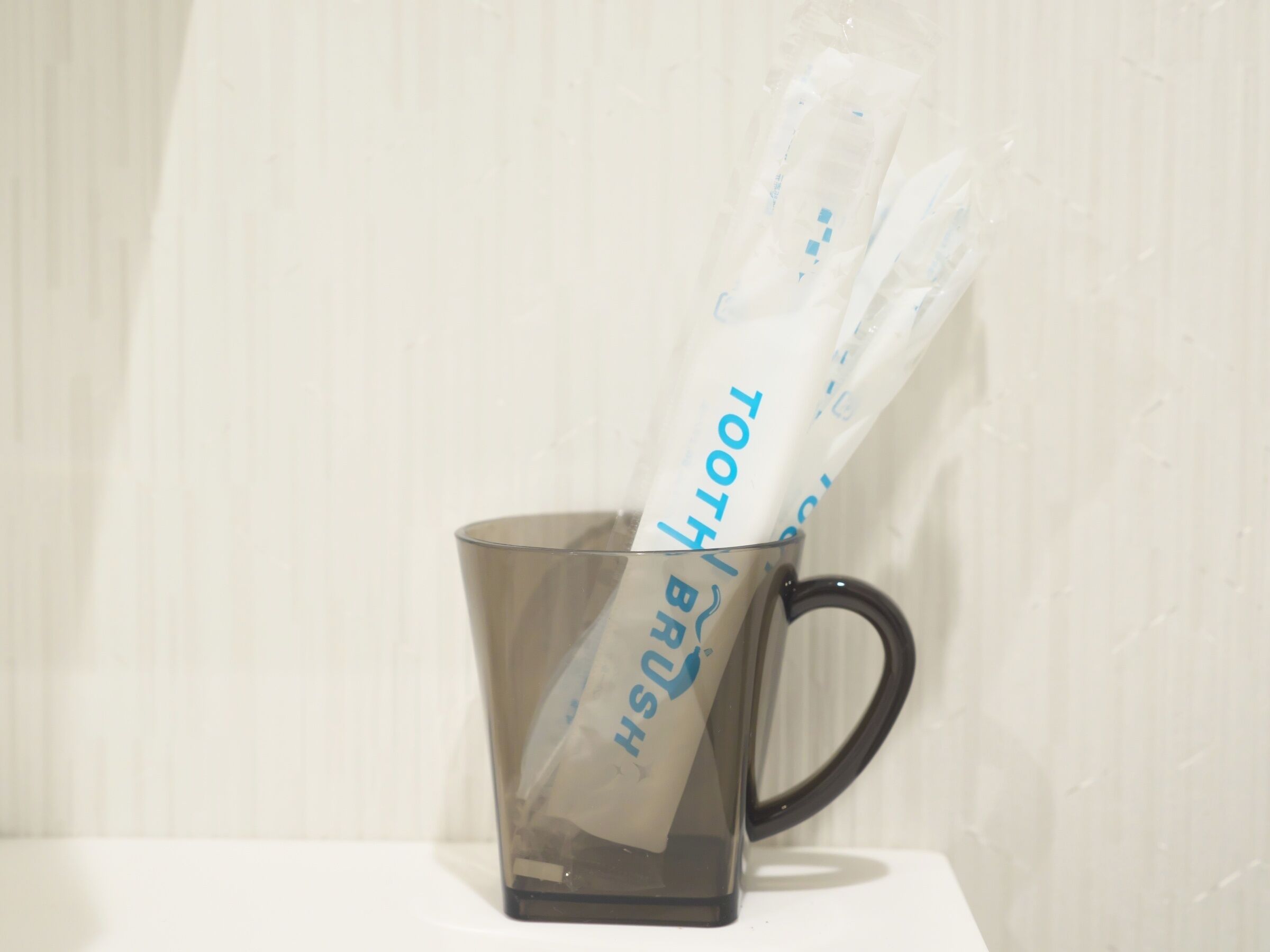 Una taza de vidrio transparente con asa negra sobre una superficie blanca.