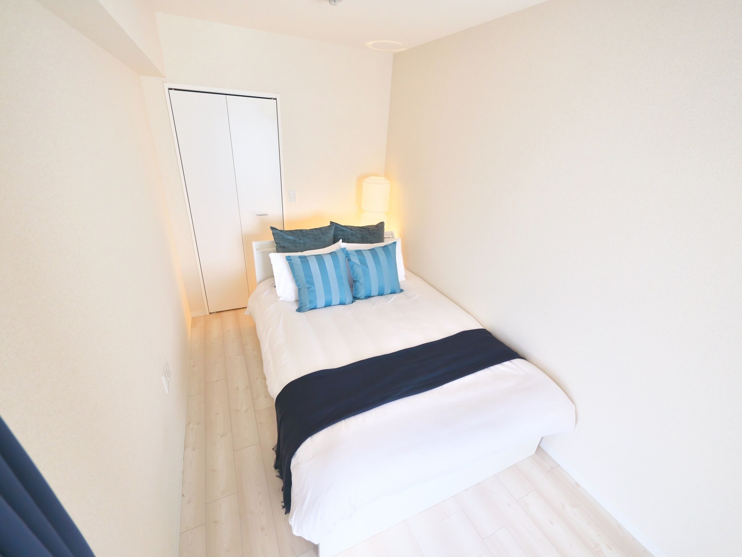 Een kleine hotelkamer met een bed, een bedlamp en een deur.