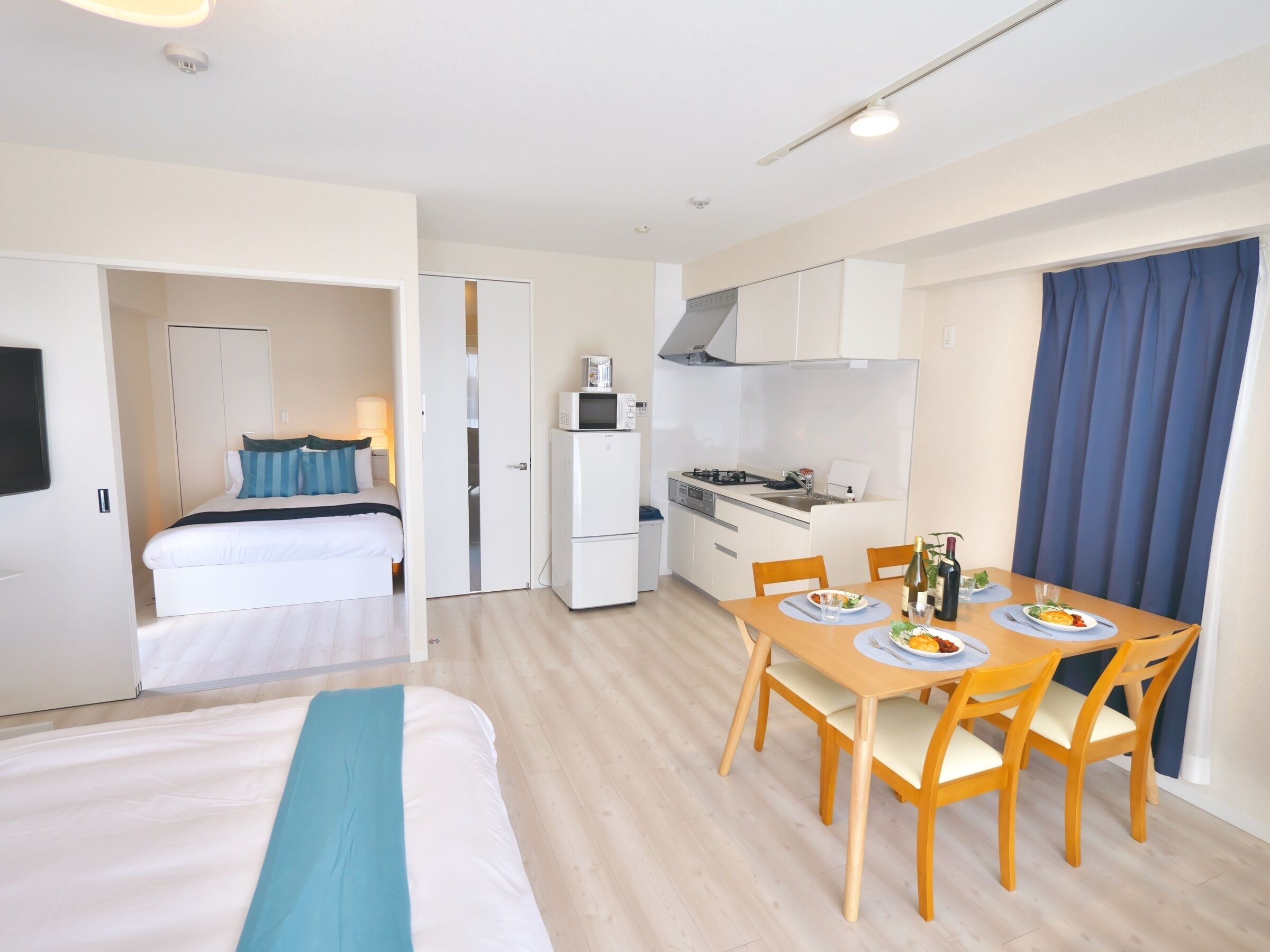 A compact hotel room with a bed, a small kitchenette, and a dining area with a table and chairs.