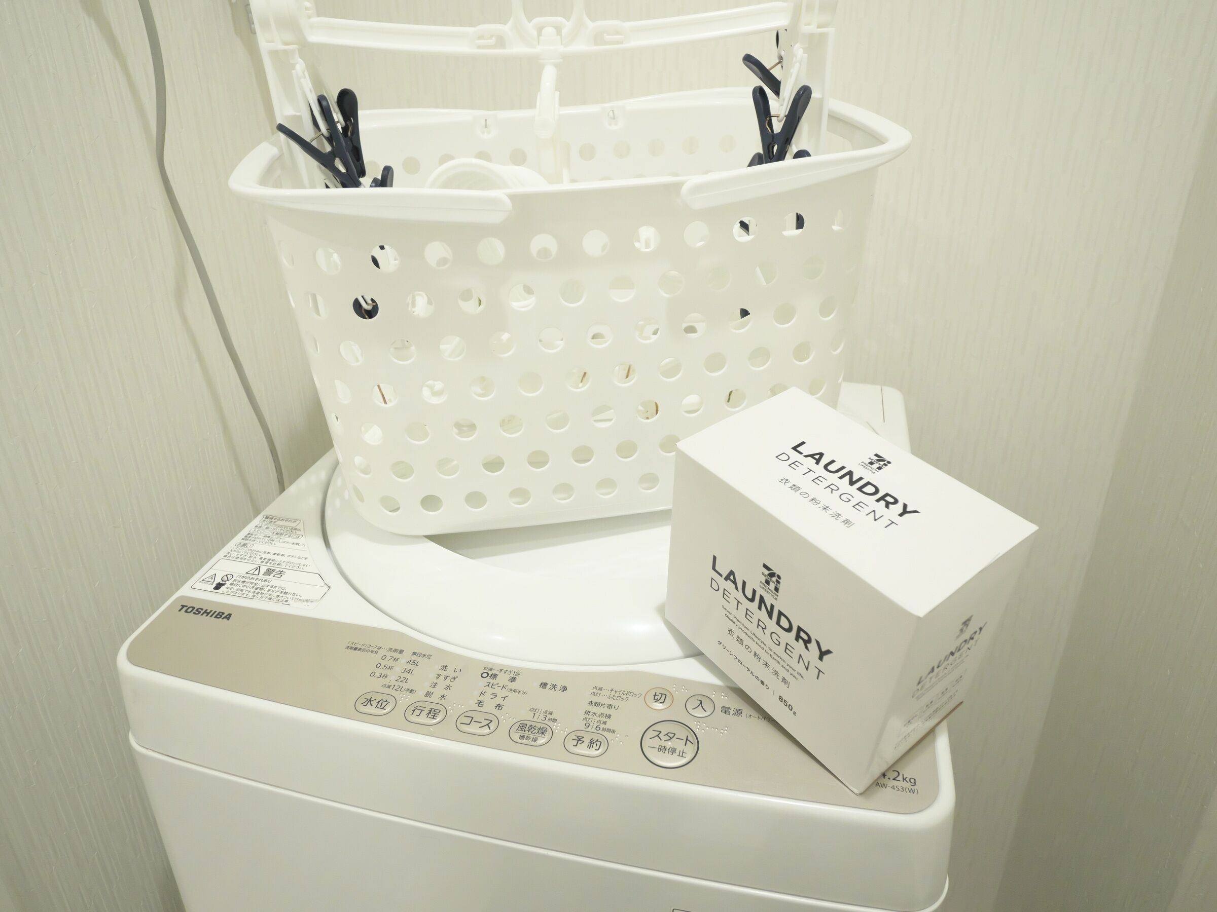 A white washing machine with a control panel and a white laundry basket with clips on top.