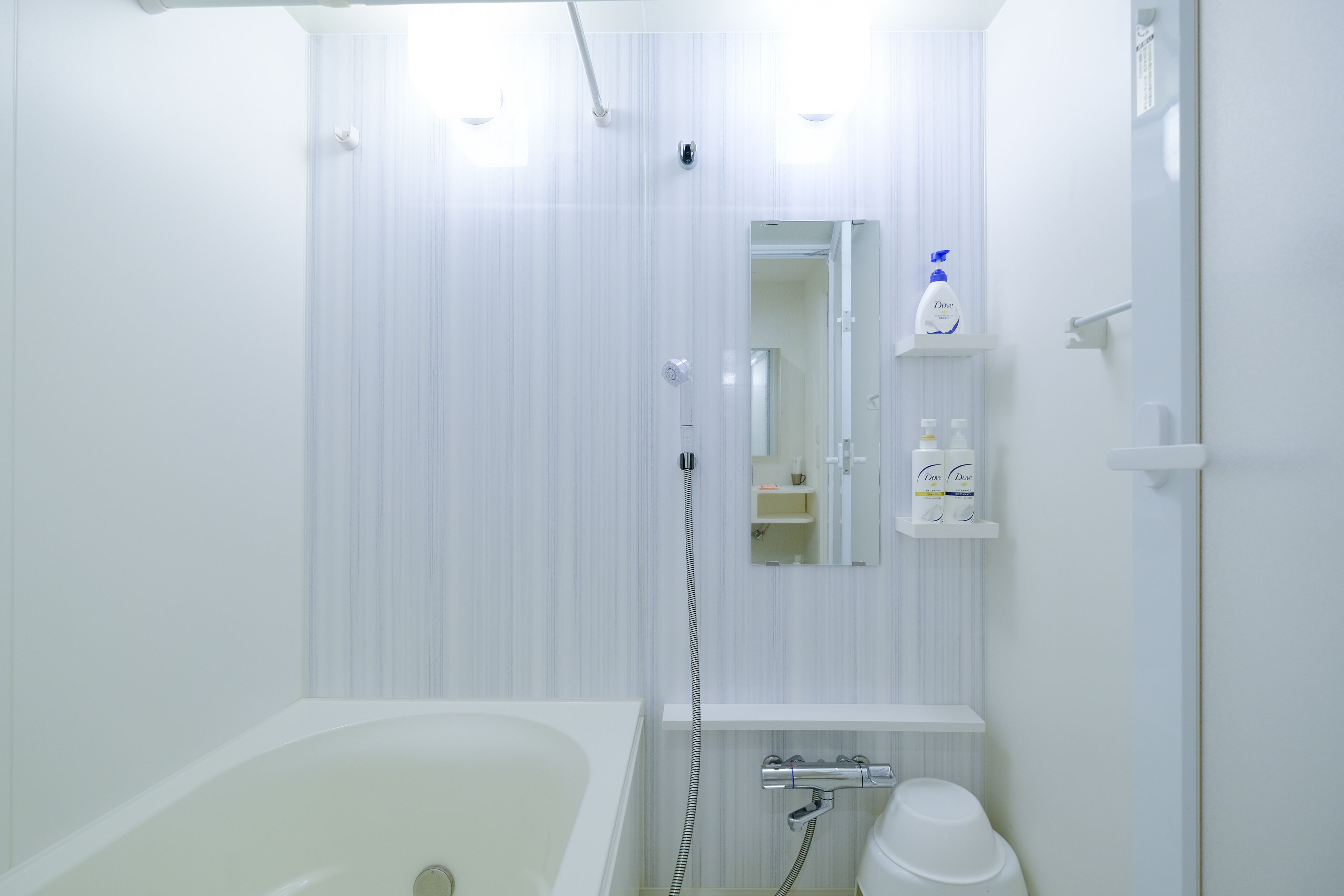 Et badeværelse med badekar, bruser og toilet. Der er et spejl over vasken, og en hylde med toiletartikler.